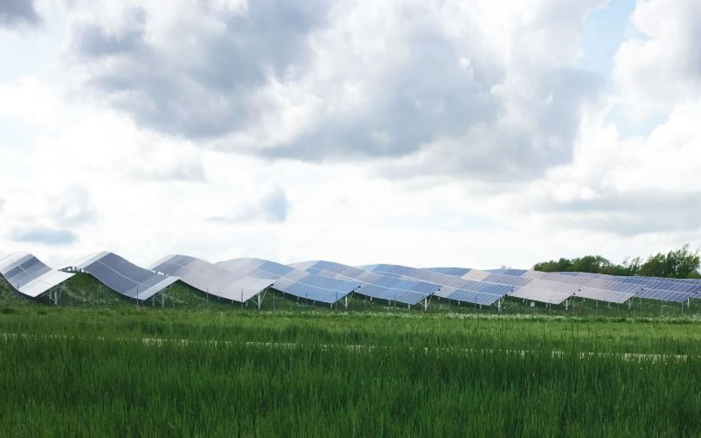 Solar panels installed in a grassy field, set against a backdrop of a cloudy sky.